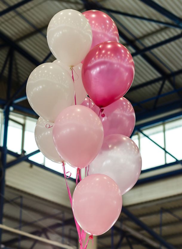 Traube weisser und rosafarbener Ballons mit Helium gefüllt, schweben in einer Messehalle
