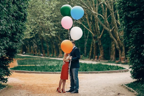 Ein verliebtes Paar im Park küsst sich hinter einer Traube bunter Heliumballons